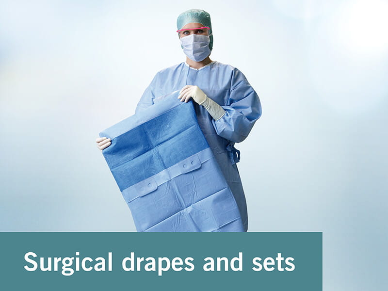 Person dressed in operation gown wearing a face mask, surgical gloves and a surgical cap while holding a surgical drape