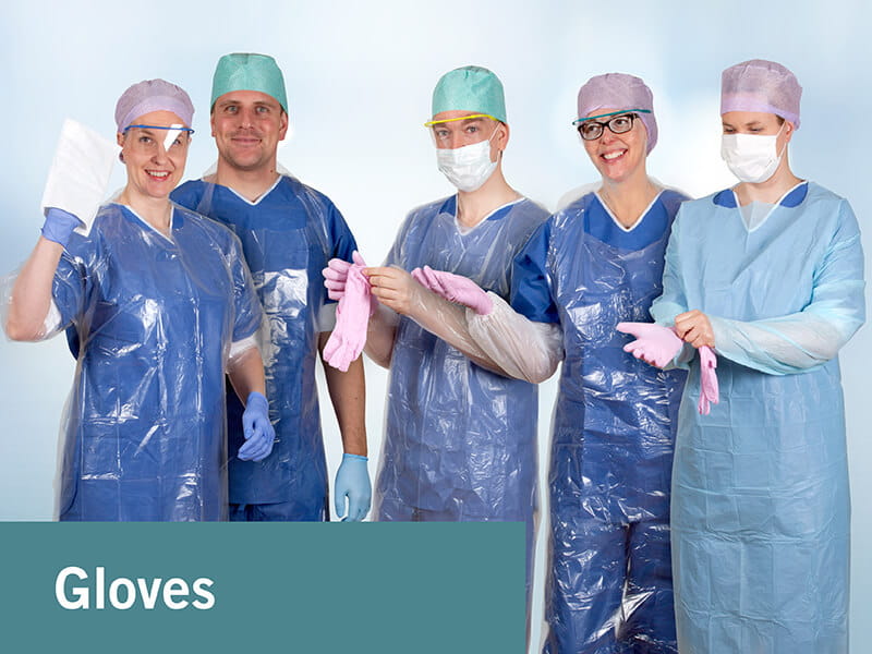 Five persons dressed in scrub suits putting on examination gloves and wearing protective gowns, surgical caps and face masks