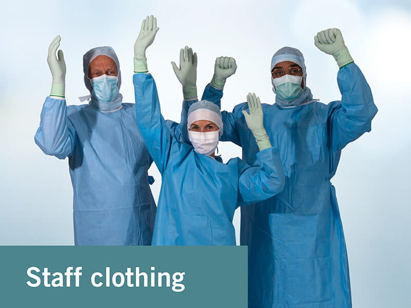 three persons dressed in operation gowns wearing surgical hoods, face masks and surgical gloves